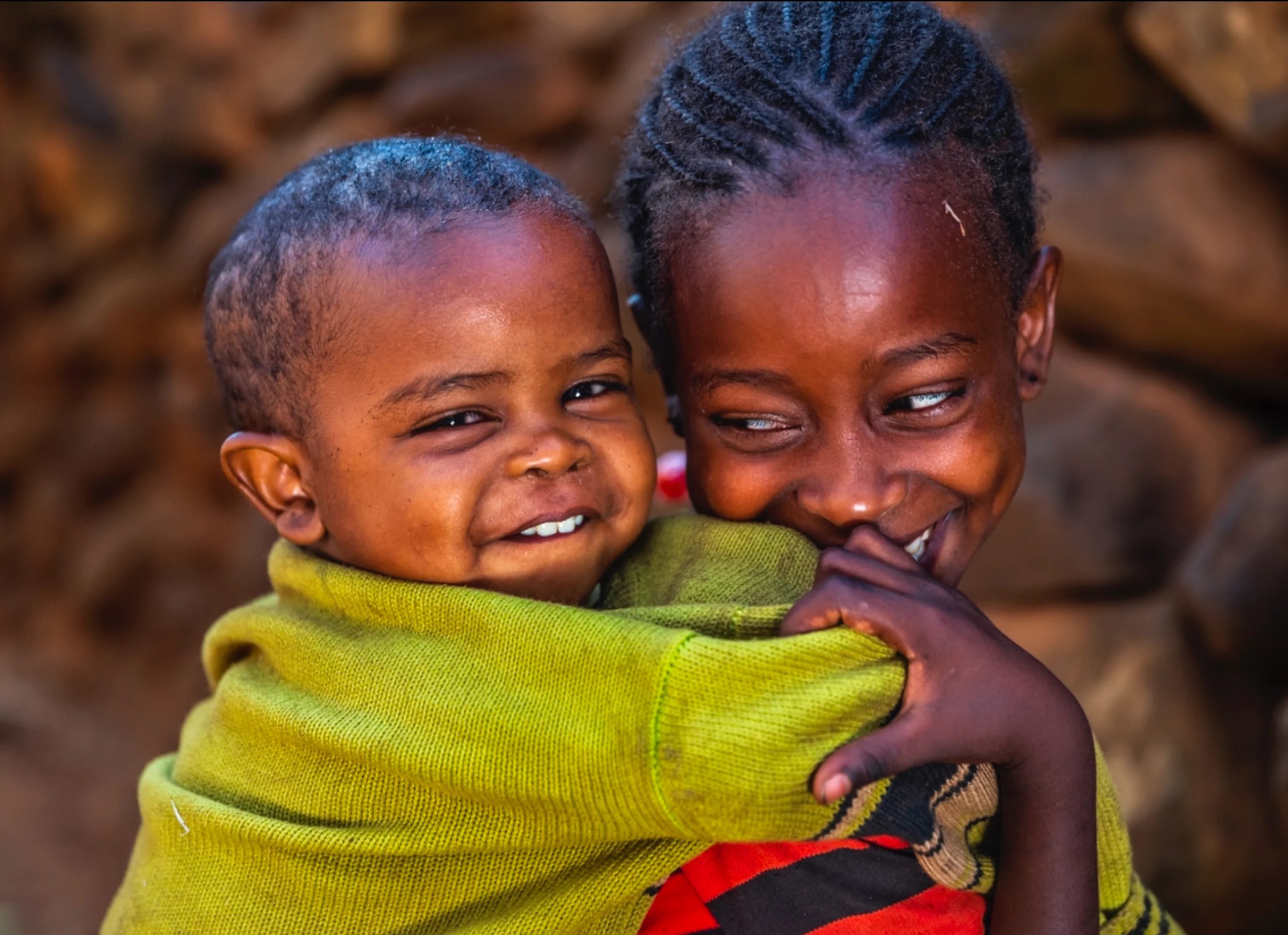 Two smiling children sharing a joyful moment outdoors