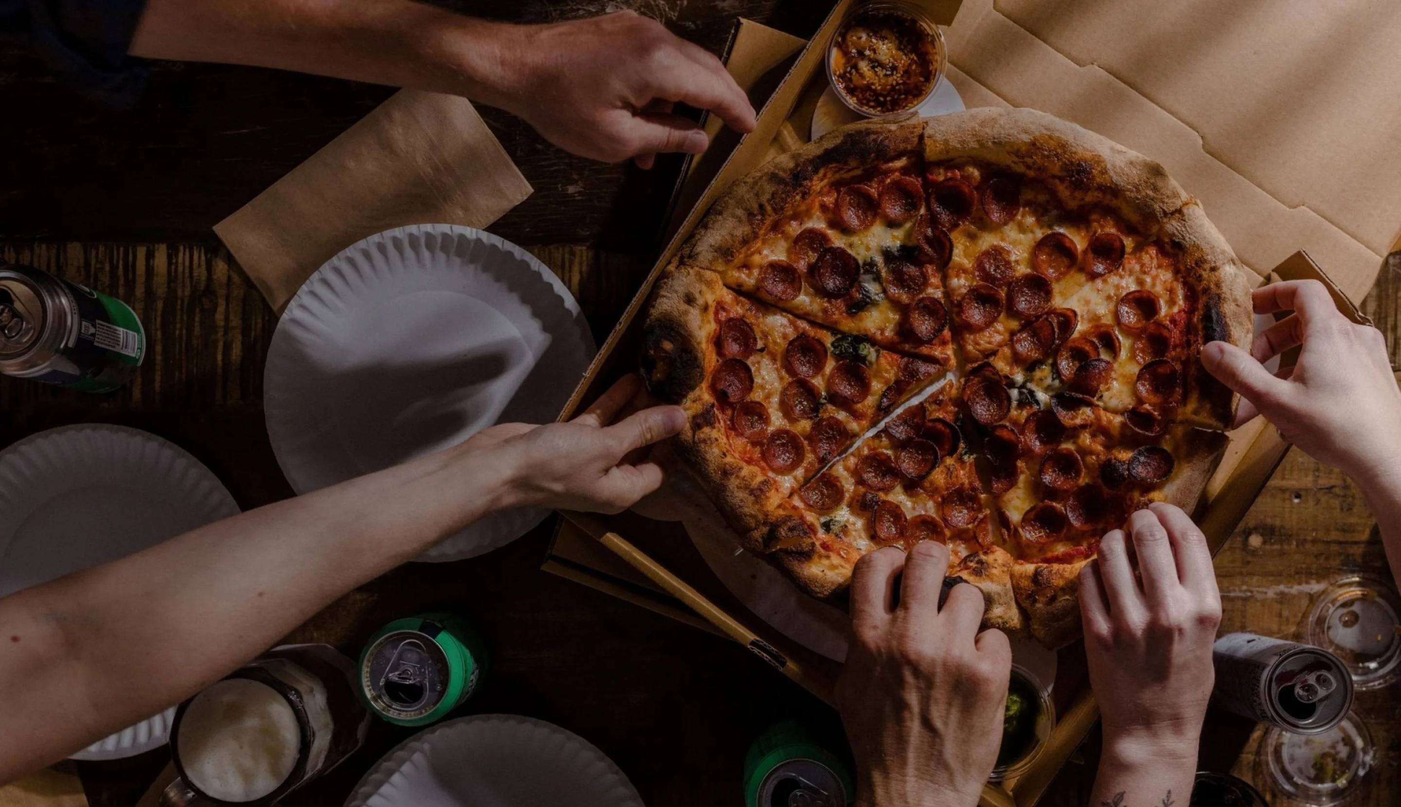 Pepperoni pizza served in a box with friends sharing slices