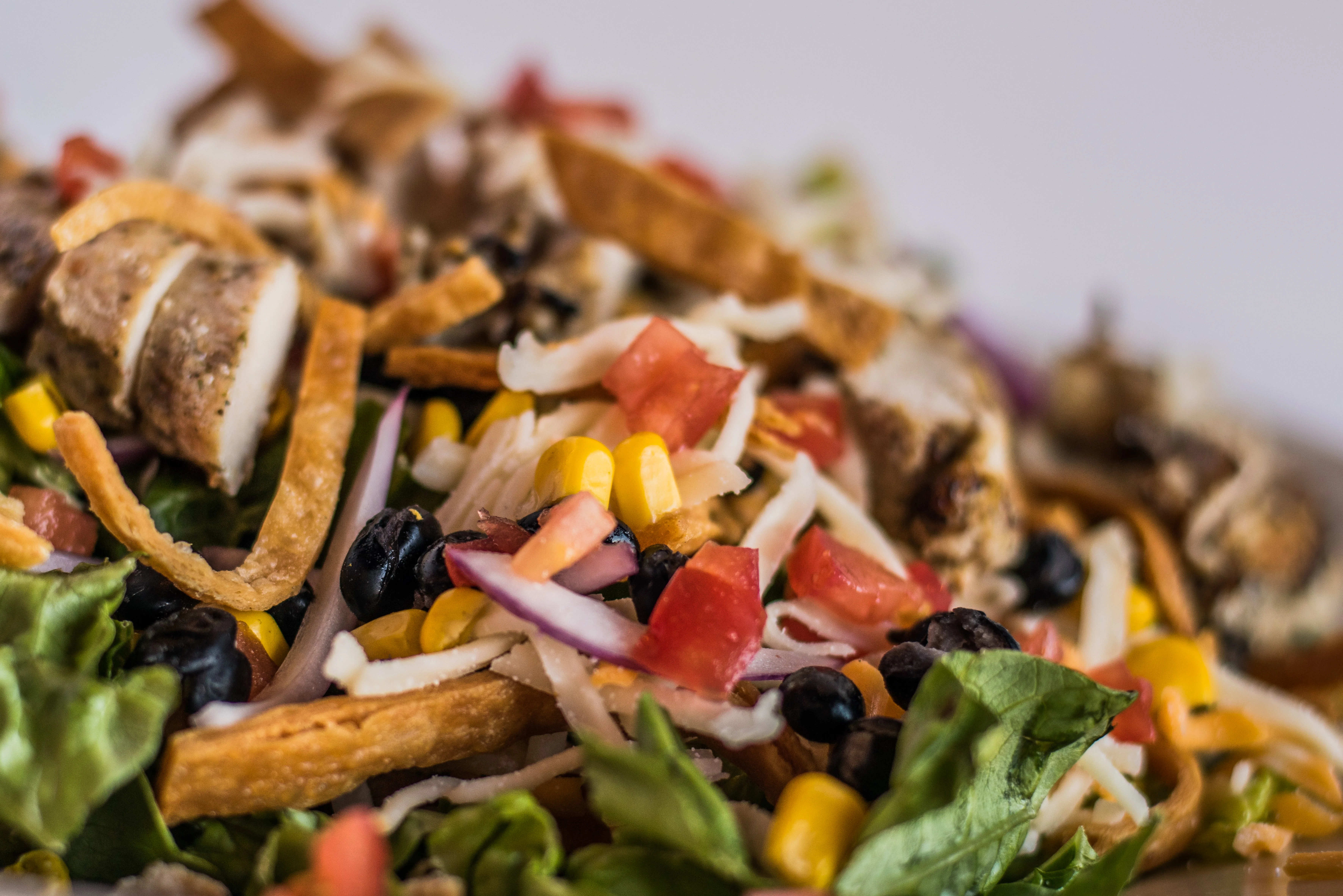 A colorful salad featuring shredded lettuce, corn, black beans, diced tomatoes, crispy tortilla strips, and cheese.