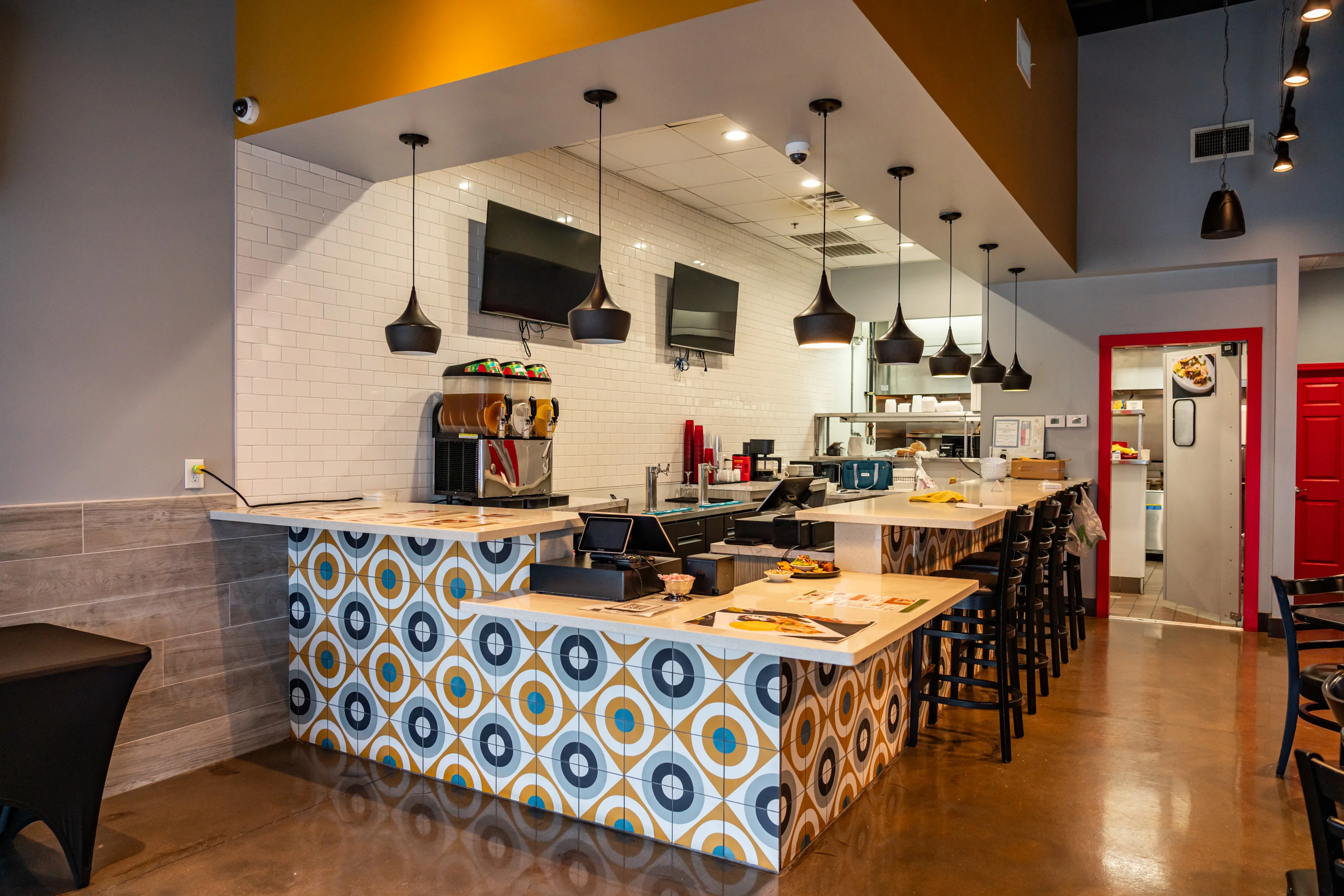 A modern restaurant interior showcasing a stylish counter with seating, colorful decor, and kitchen elements visible.