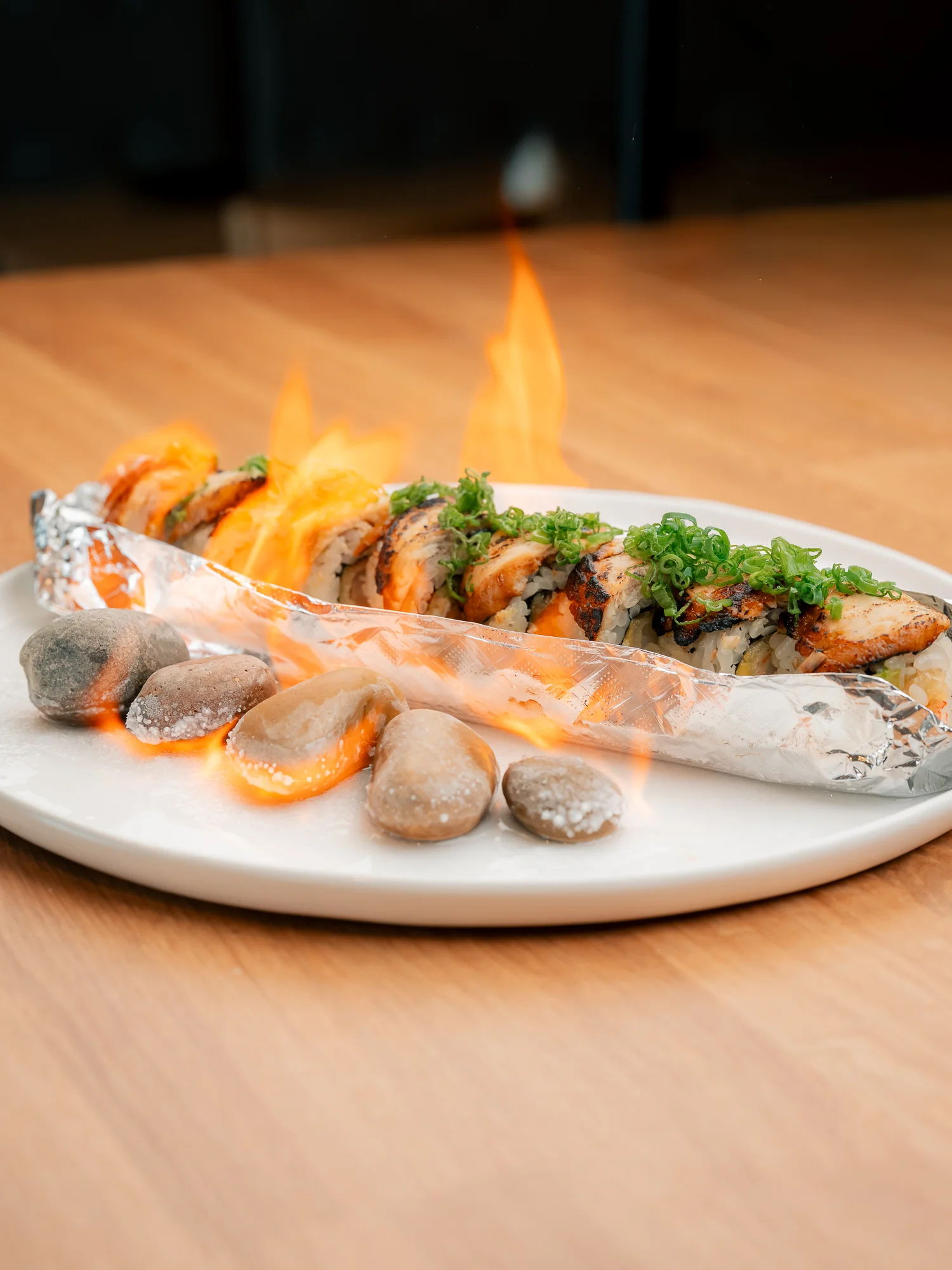 Flaming sushi roll served on a plate with decorative stones