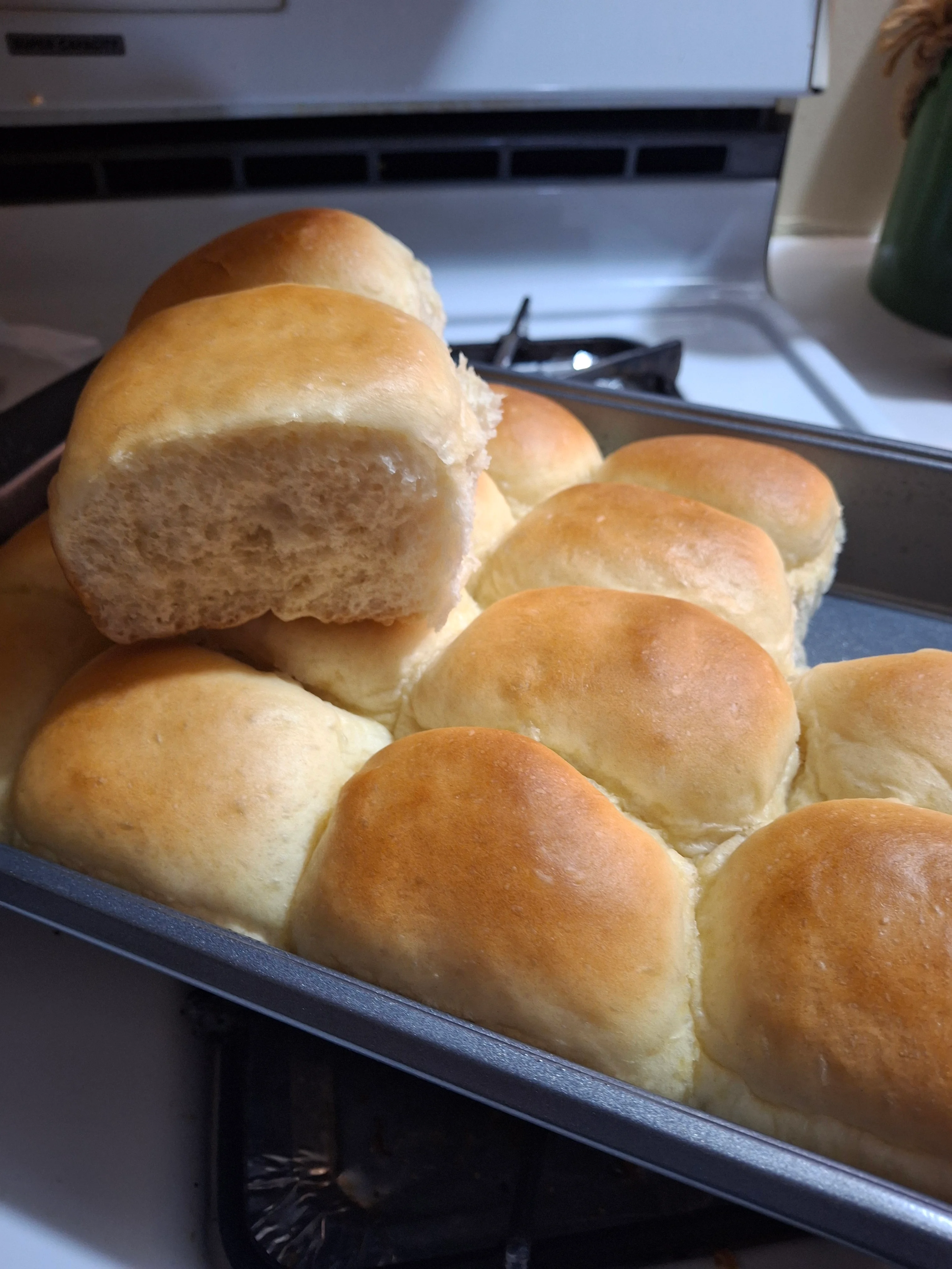 Freshly baked dinner rolls stacked in a pan, golden brown on the top with a soft and fluffy interior.