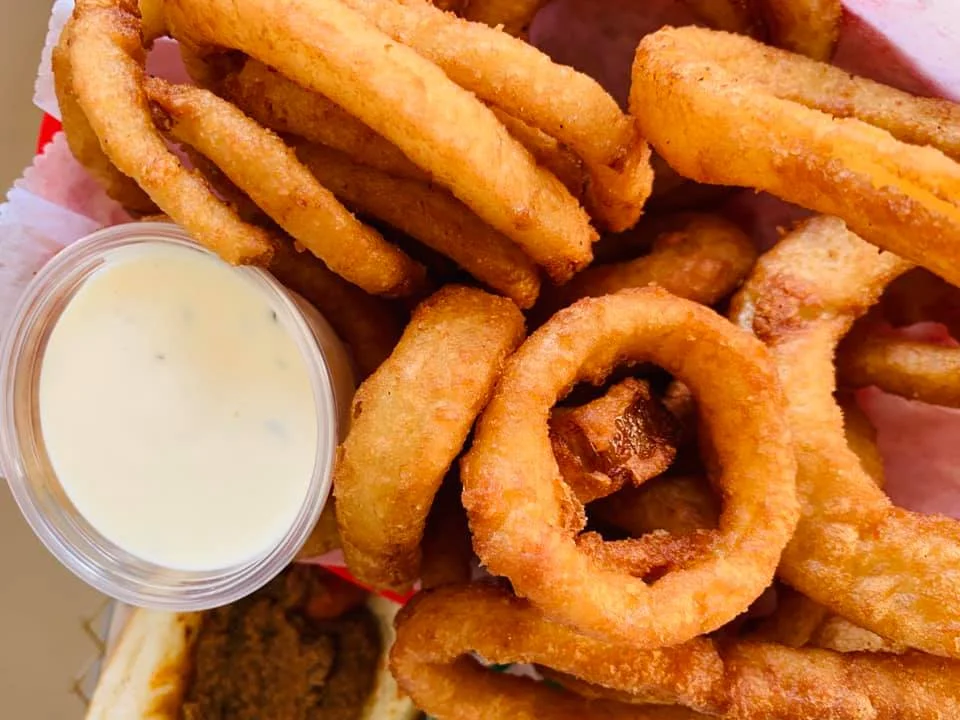 A serving of crispy onion rings accompanied by a small container of dipping sauce.