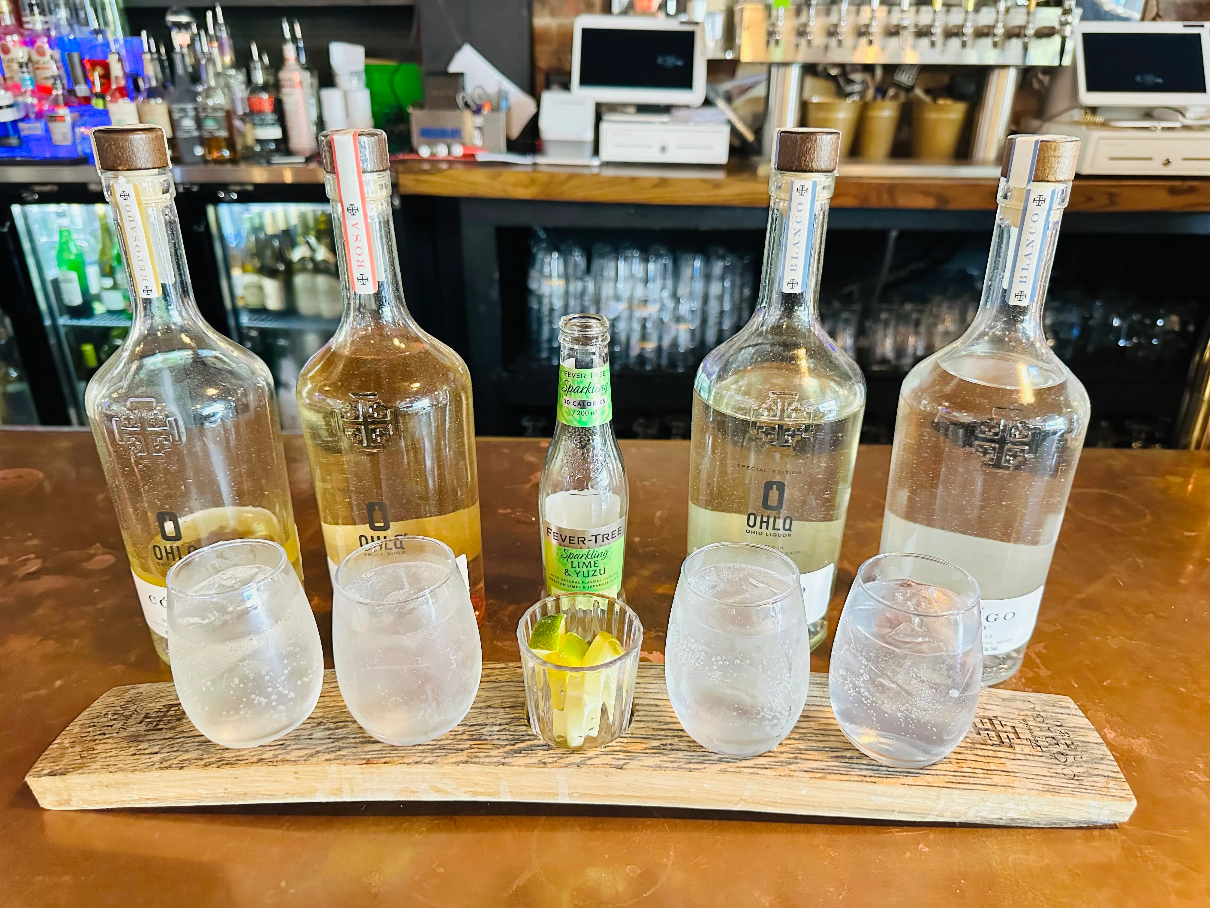A selection of liquor bottles showcased on a bar, accompanied by glasses filled with sparkling water and lime on a wooden board.