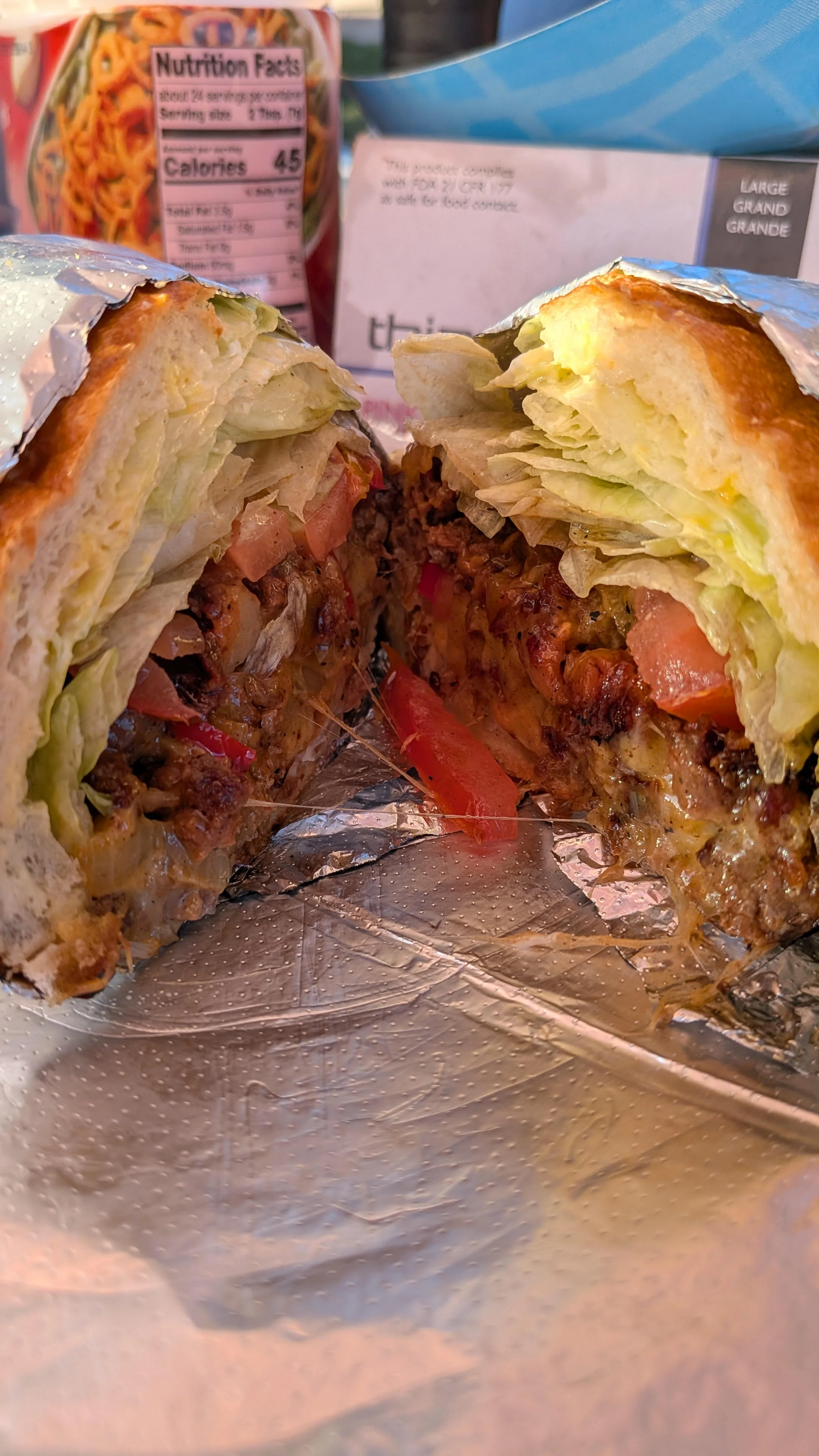 A chopped cheese sandwich cut in half, revealing melted cheese and various toppings inside a soft bun.