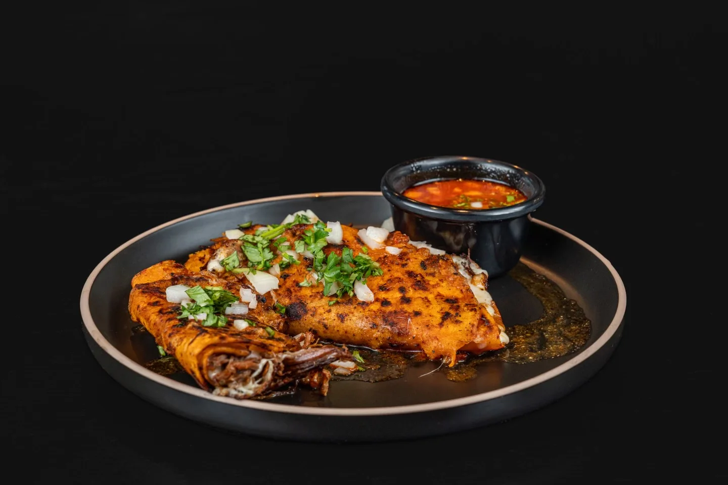 A dish featuring two corn tortillas filled with meat, garnished with onions and cilantro, served with a side of salsa.