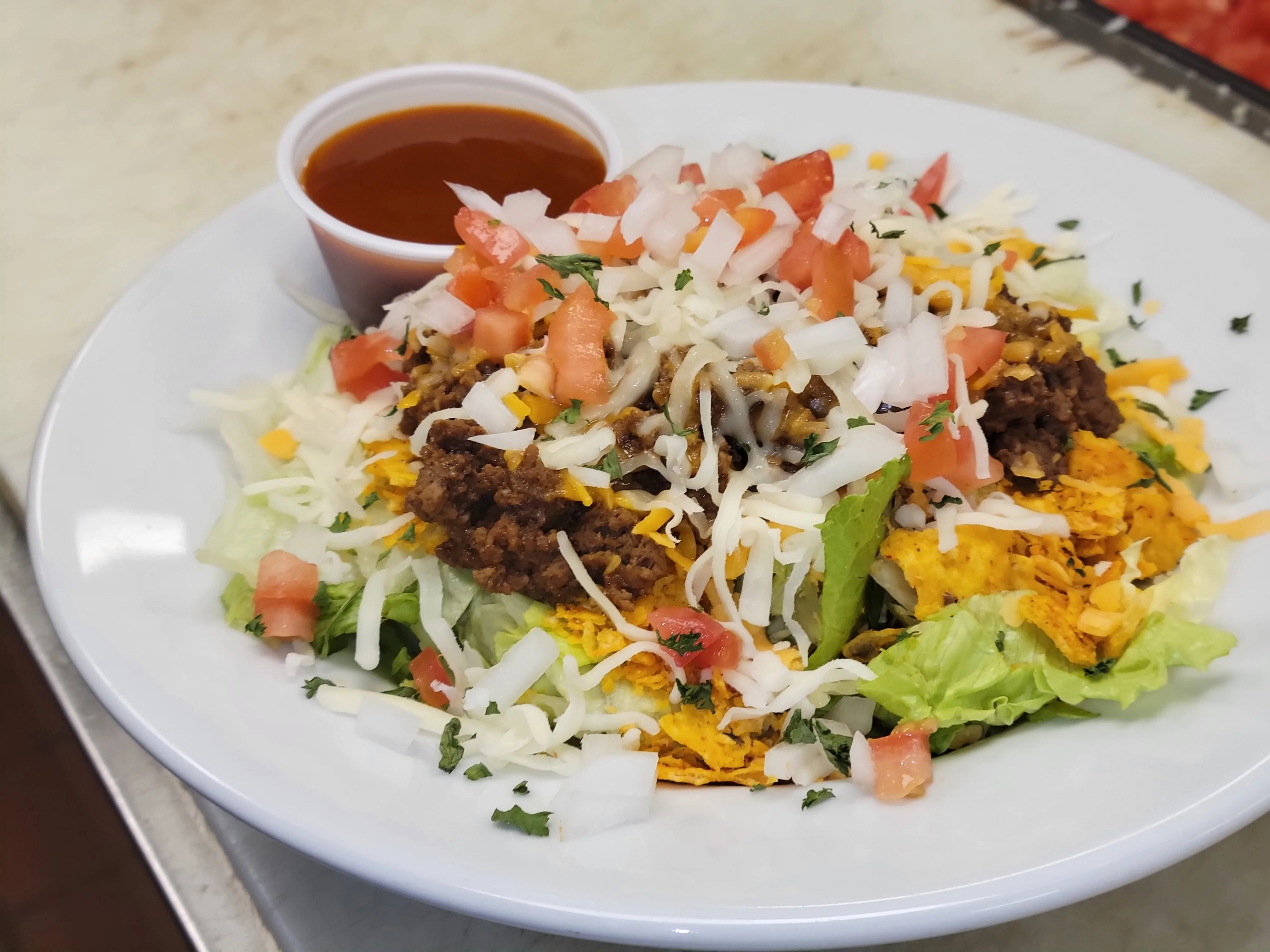 A colorful plate of nachos topped with seasoned ground beef, cheese, lettuce, tomatoes, and a side of sauce.