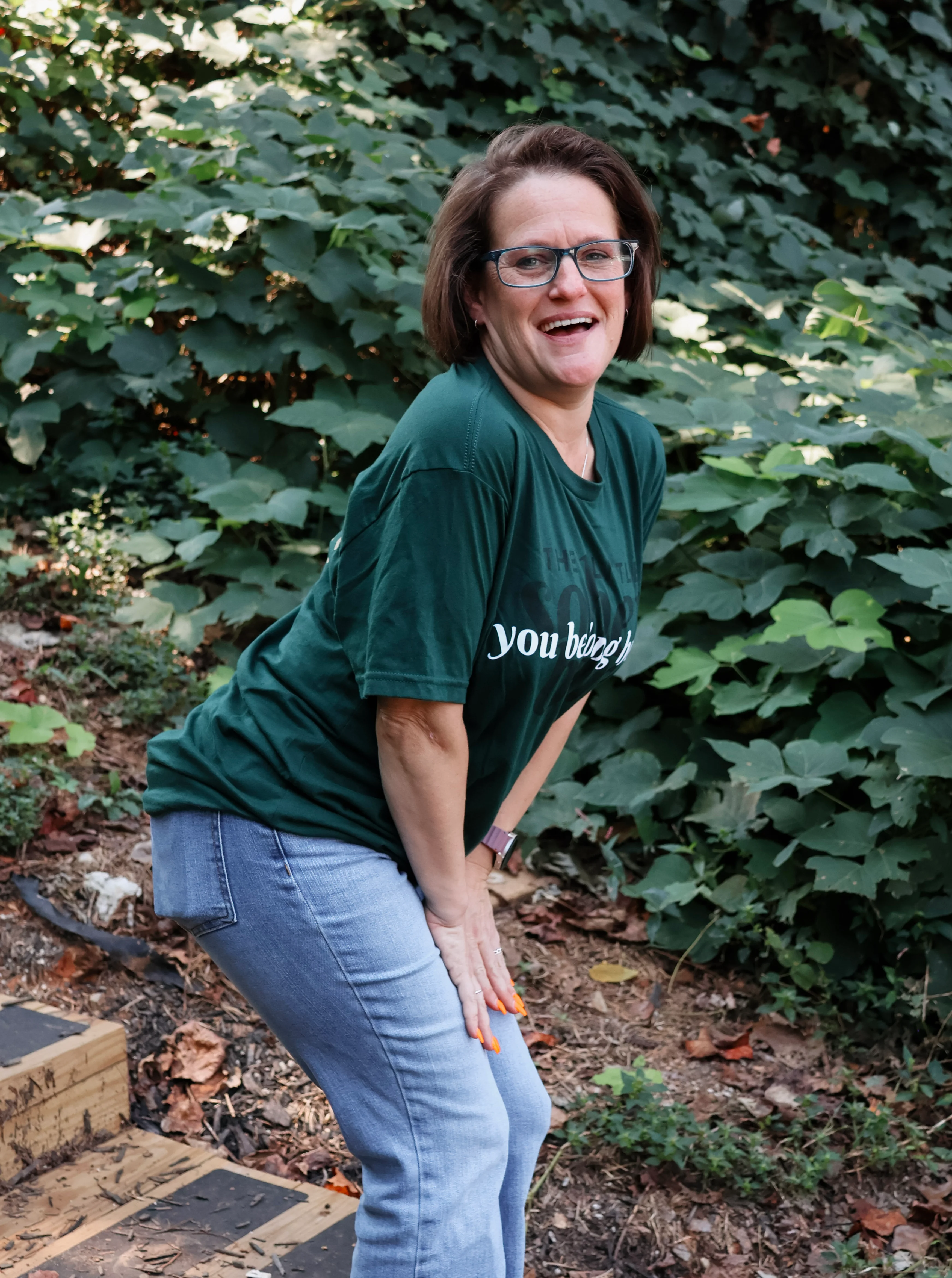 Smiling woman raising her hand outdoors in front of lush greenery