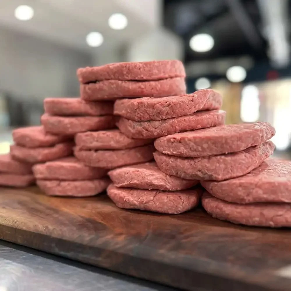 Freshly formed hamburger patties stacked on a wooden board