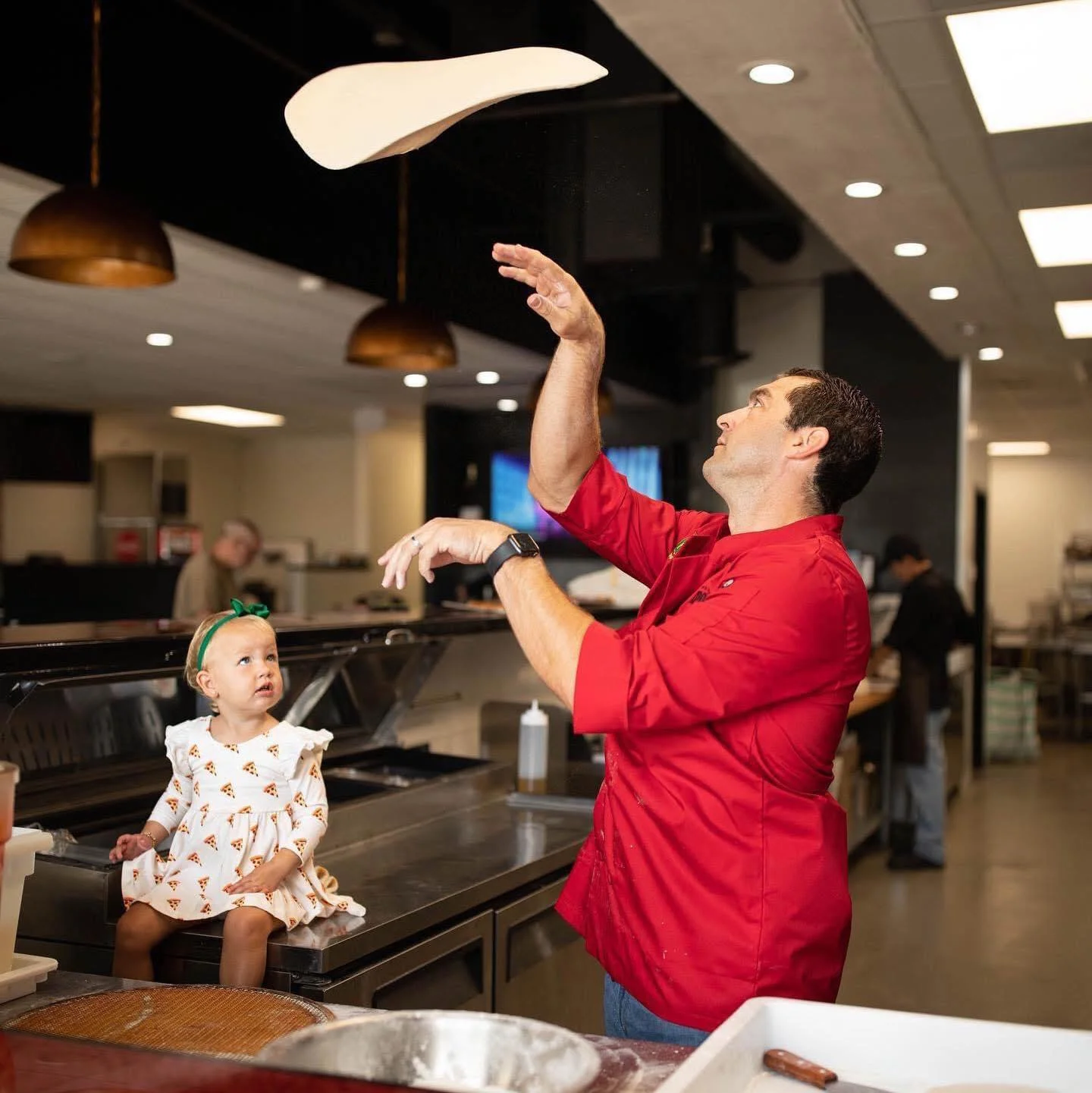 A child and parent making pizza together in a kitchen.