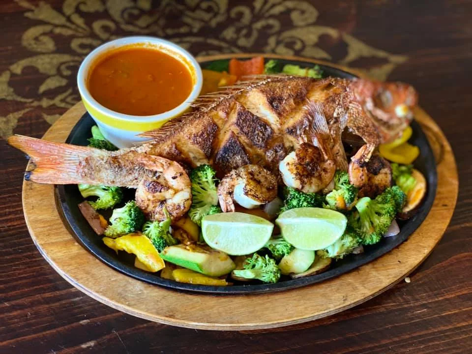 Grilled whole fish with shrimp and vegetables on a sizzling platter