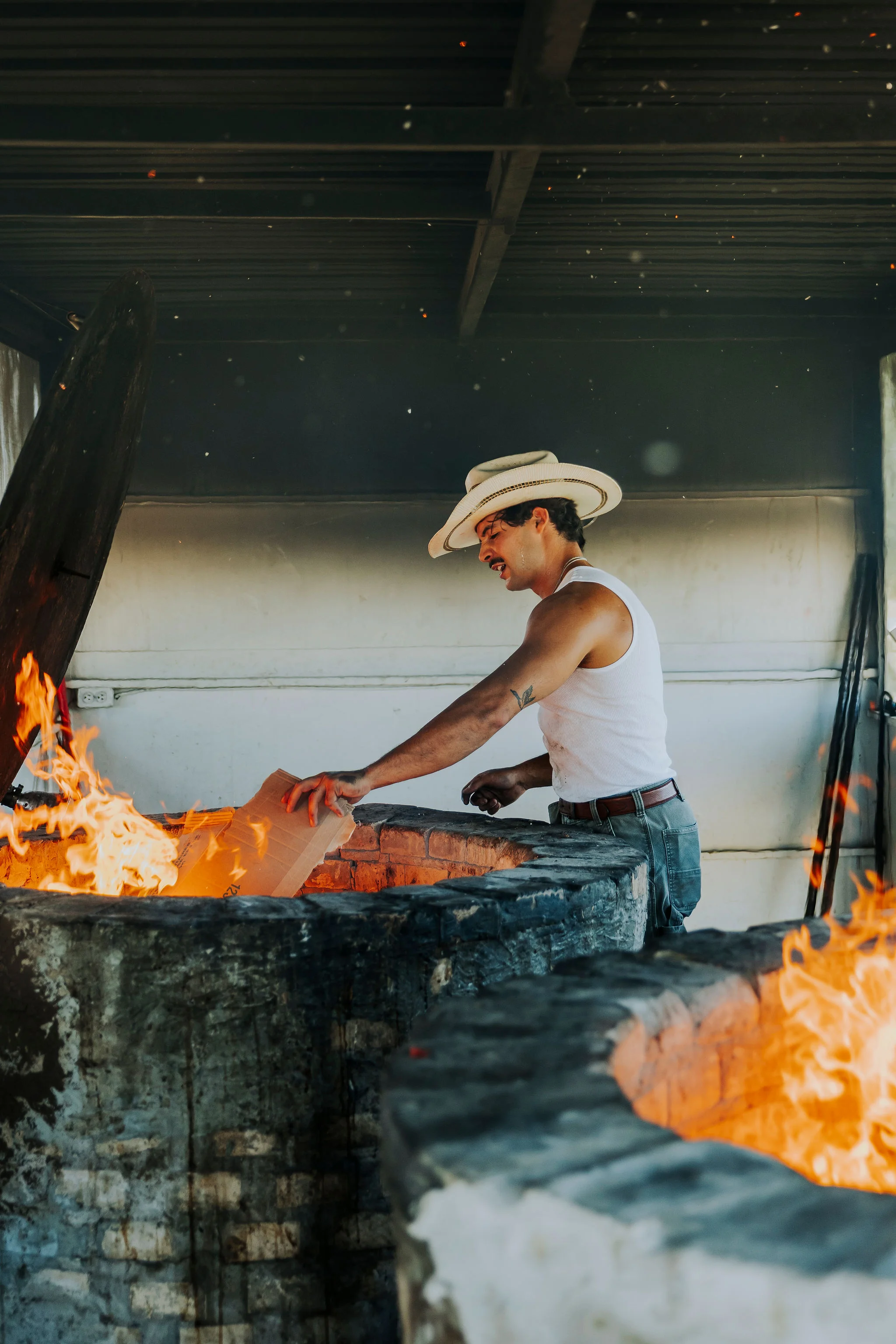 Craftsman adding wood to a traditional fire pit for cooking