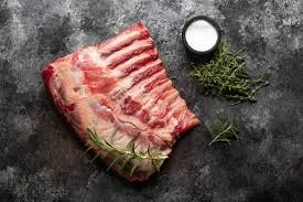 Cooked rack of lamb garnished with herbs on a white plate.