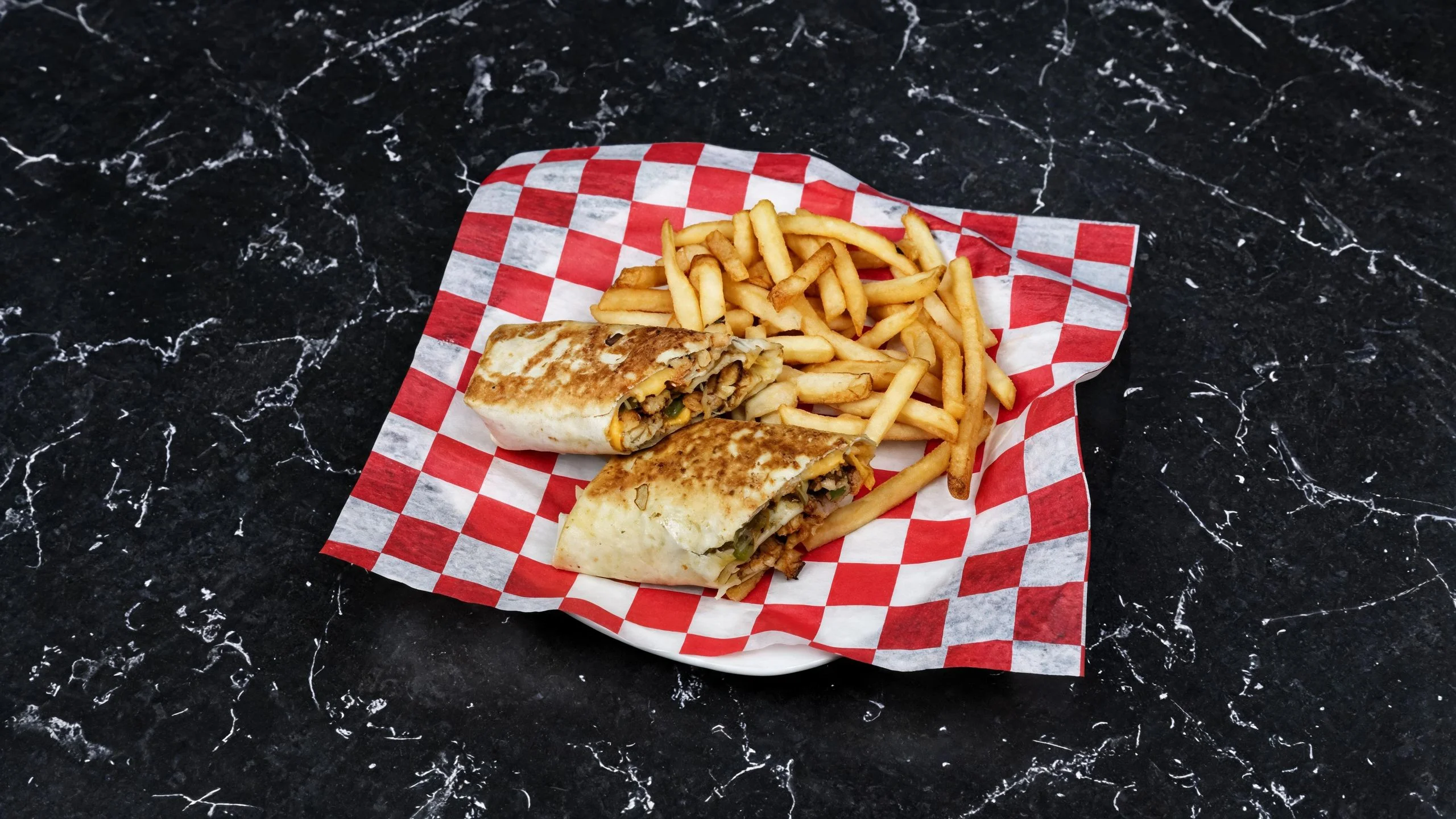 A plate with two grilled burritos accompanied by a serving of French fries, presented on a red and white checkered paper.
