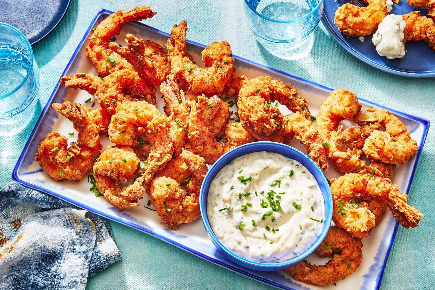 A platter of crispy fried shrimp served with a creamy dipping sauce and garnished with herbs.