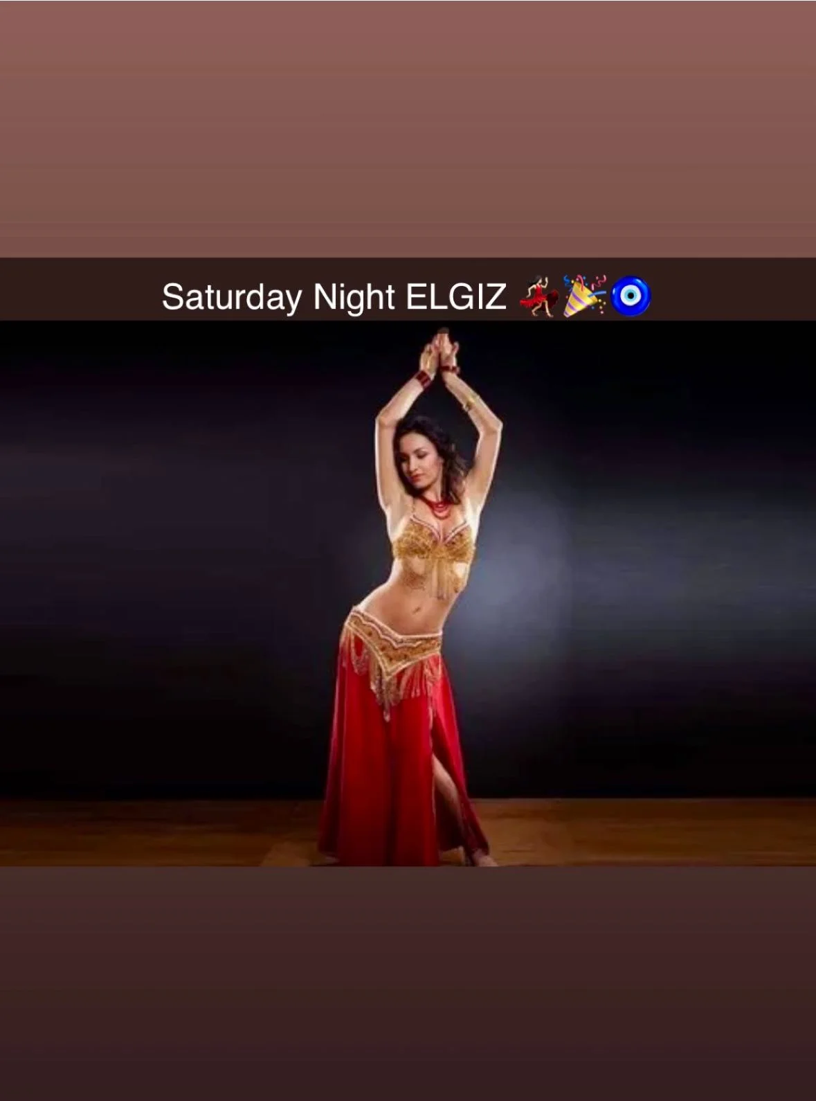 A dancer performing in a vibrant outfit featuring a golden top and a flowing red skirt, set against a dark background.