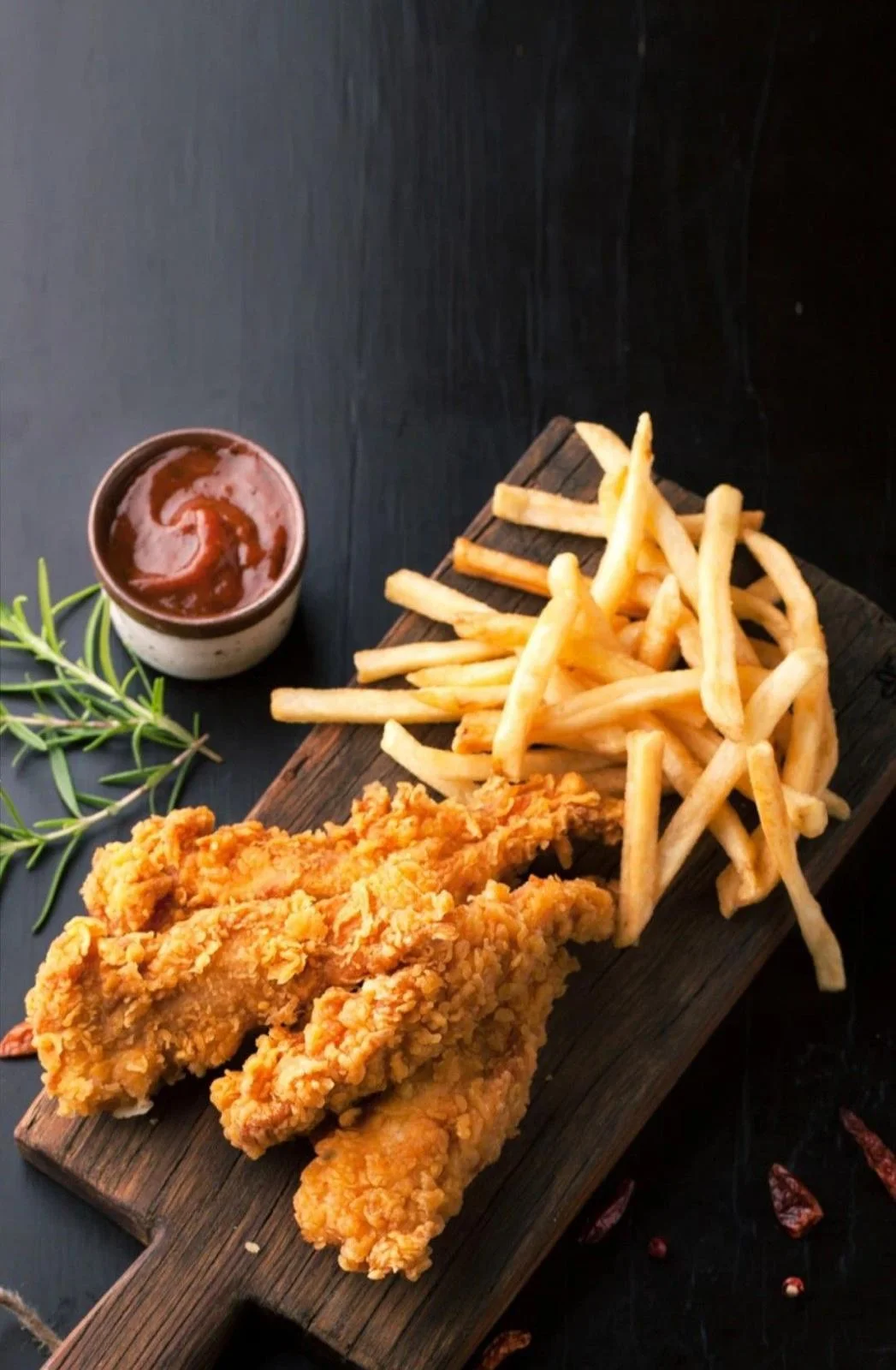 A serving of crispy fried chicken with a side of golden French fries and a small bowl of dipping sauce, arranged on a wooden platter.