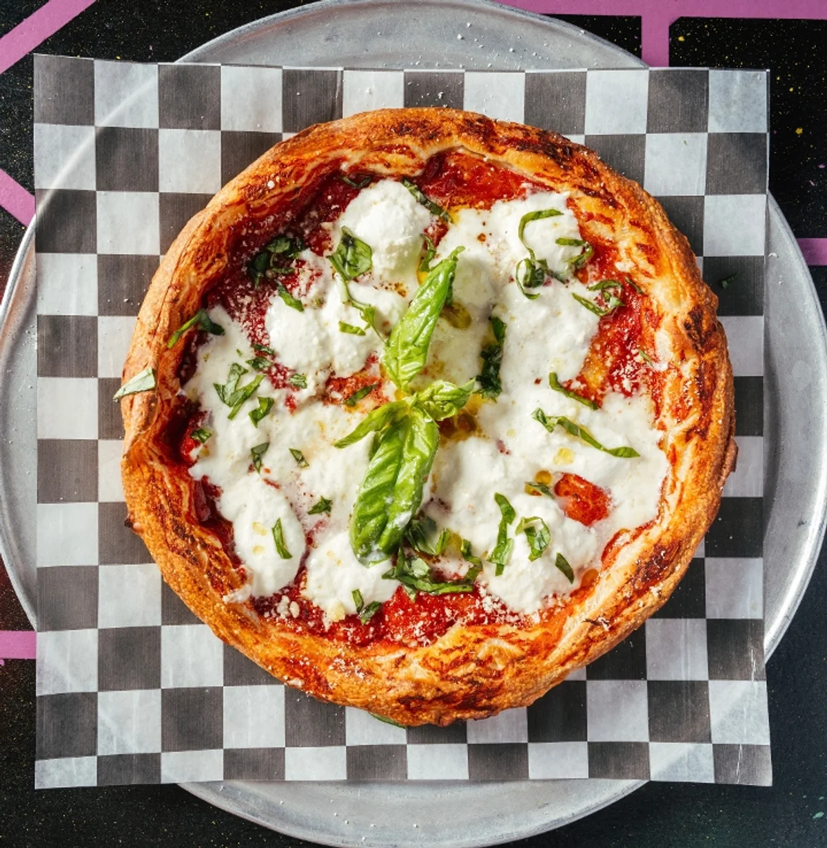 A pizza on checkered paper and a black and pink table top