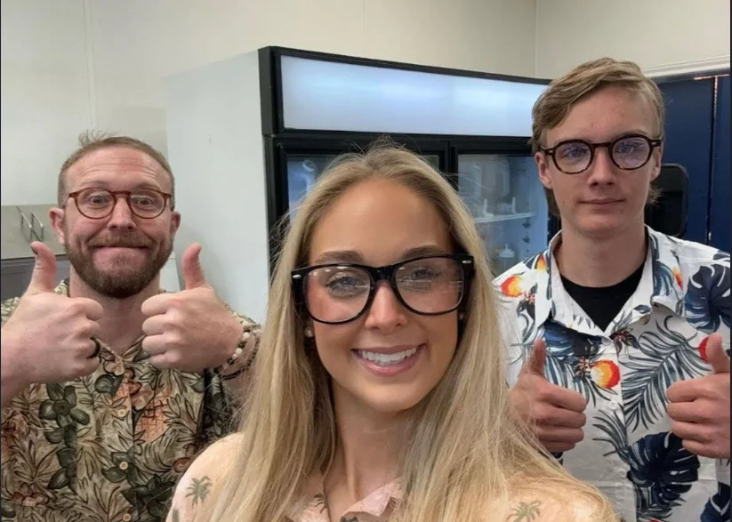 Three smiling individuals giving thumbs up in a casual setting