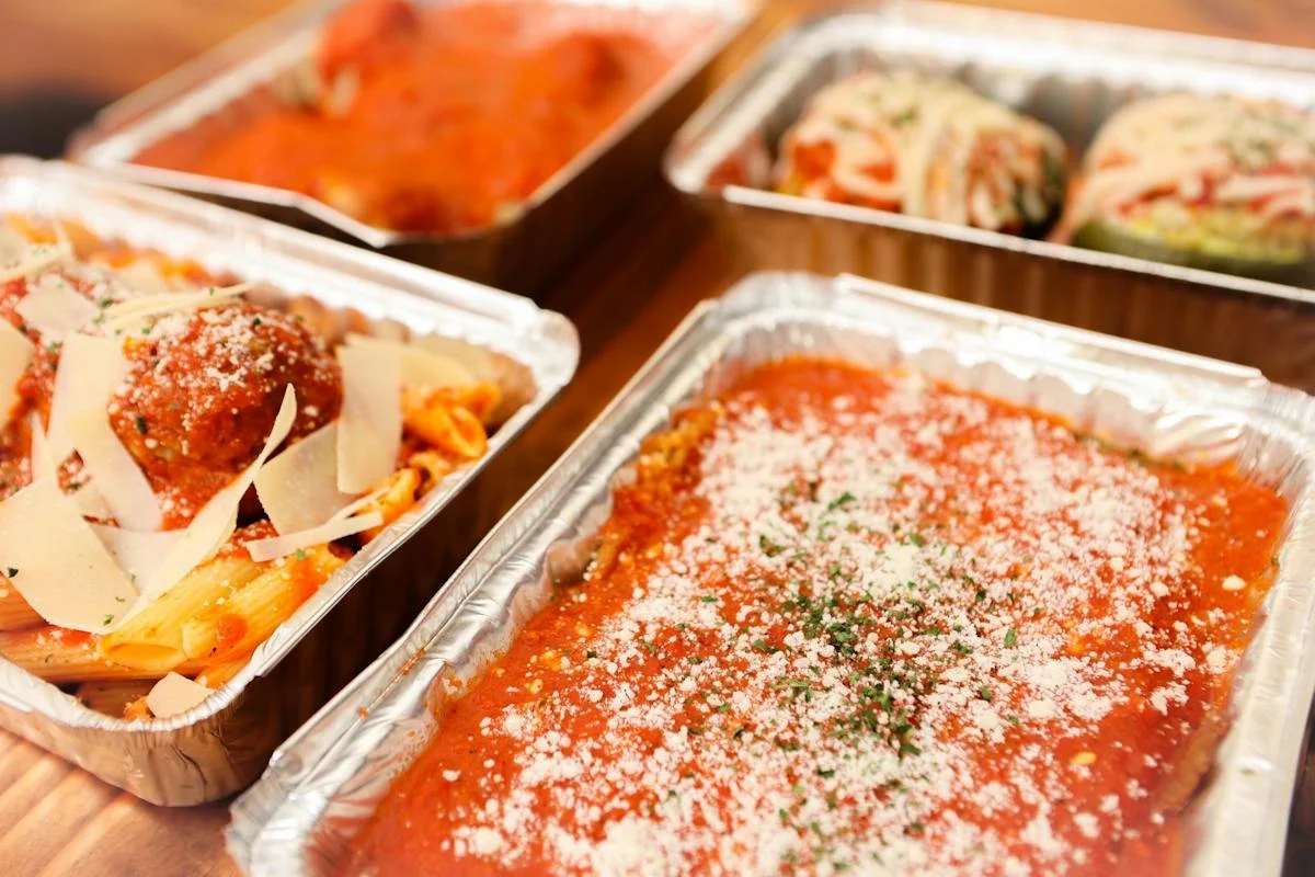 Italian pasta dishes in aluminum trays with marinara sauce and cheese