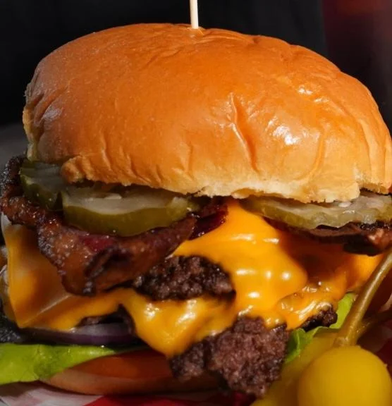 A close-up of a delicious burger featuring a toasted bun, melted cheddar cheese, crispy bacon, and pickles, all set on a colorful plate.