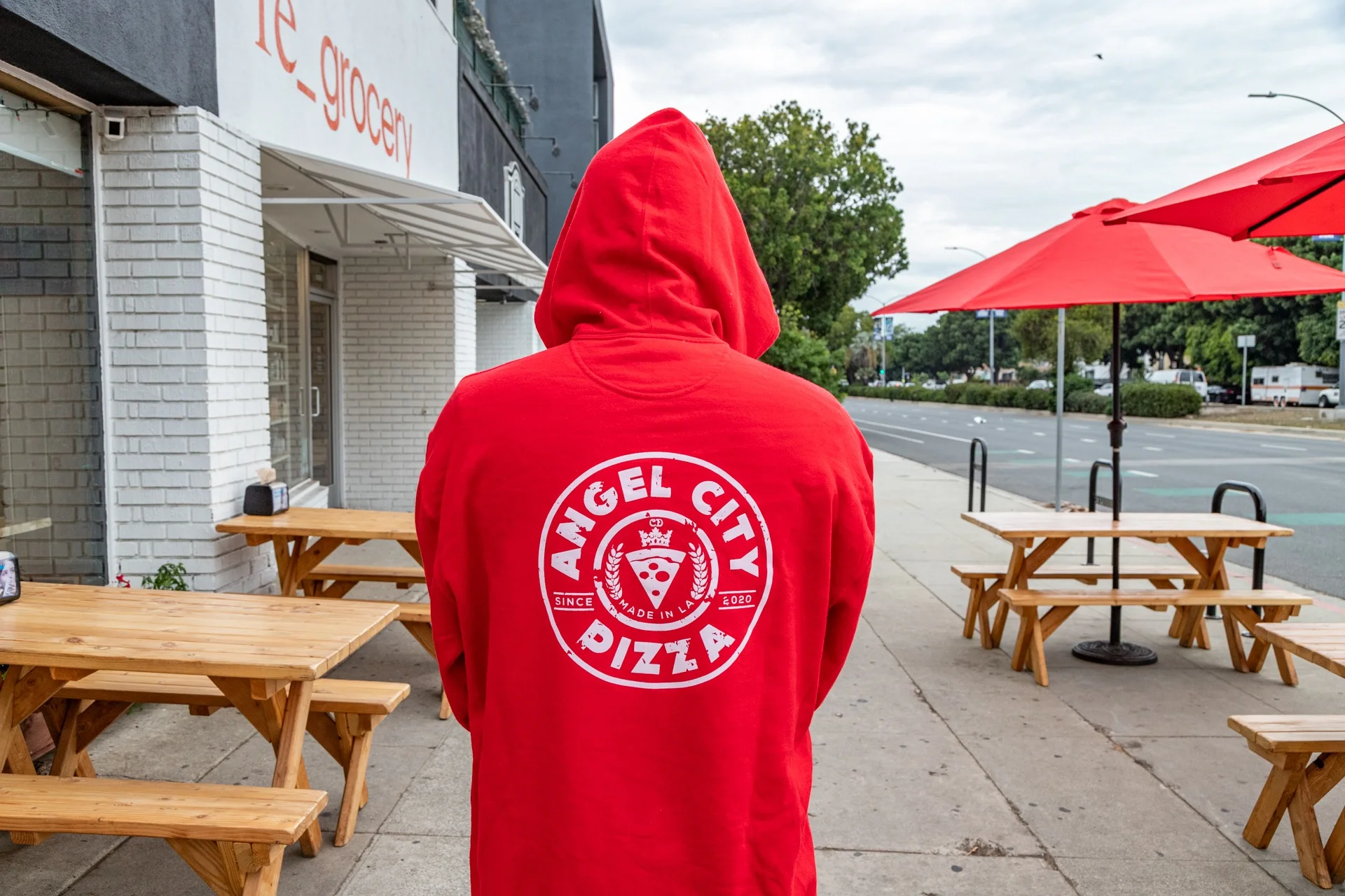 Person wearing red hoodie with Angel City Pizza logo outside a restaurant