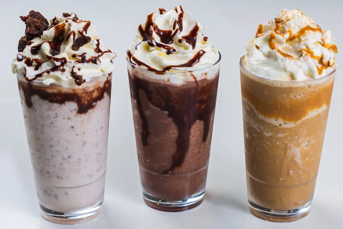 Three delicious milkshakes topped with whipped cream and chocolate drizzle.
