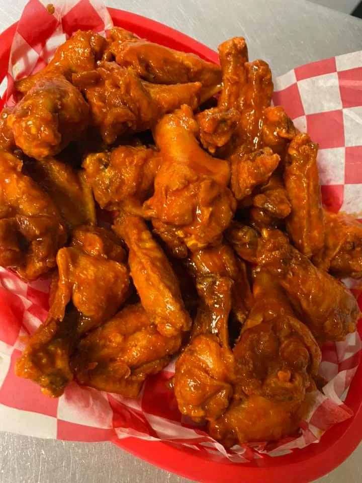 A platter of spicy chicken wings coated in a rich orange sauce.